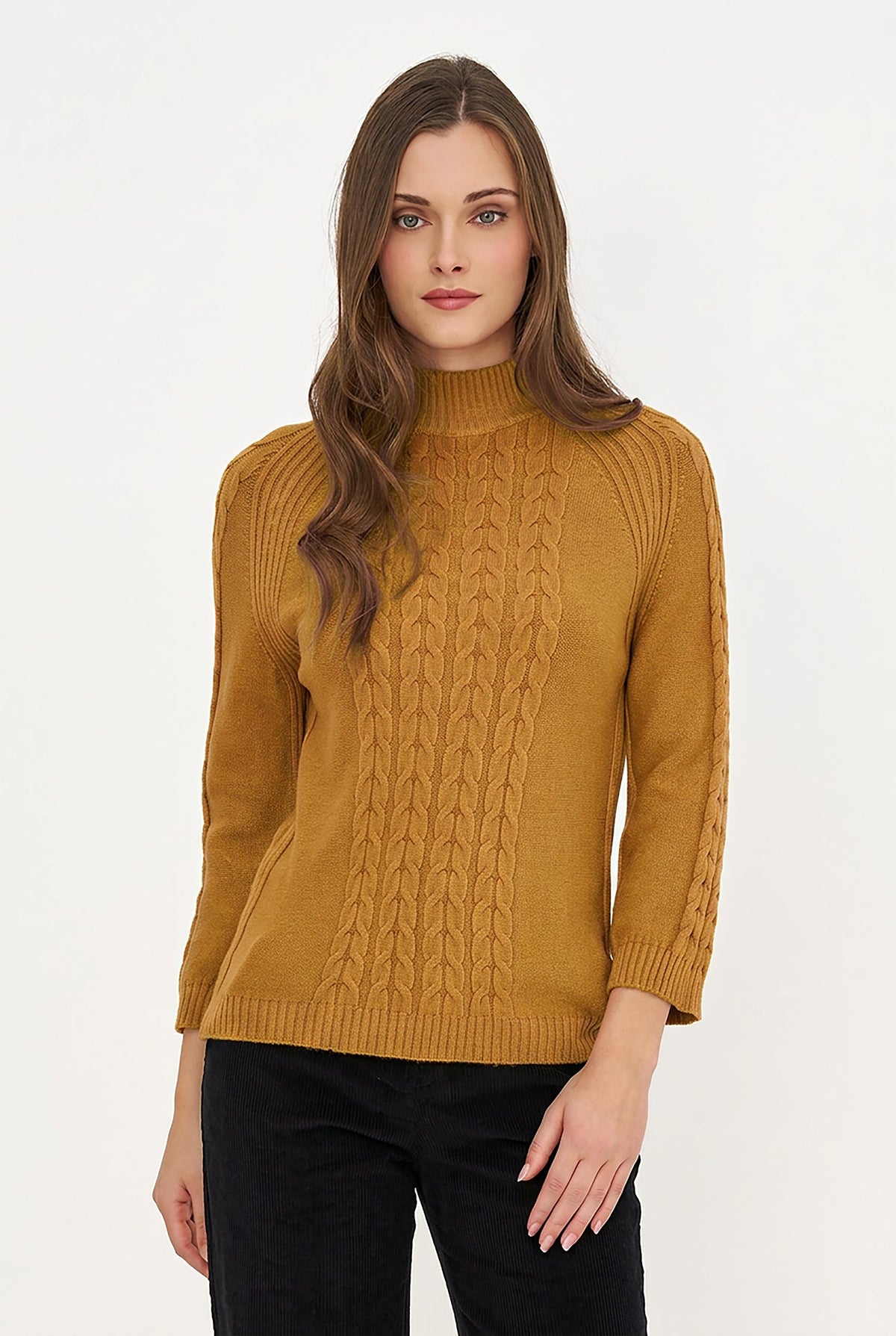 A woman modeling a mustard yellow cable-knit mock neck sweater with black pants, set against a plain white studio background.