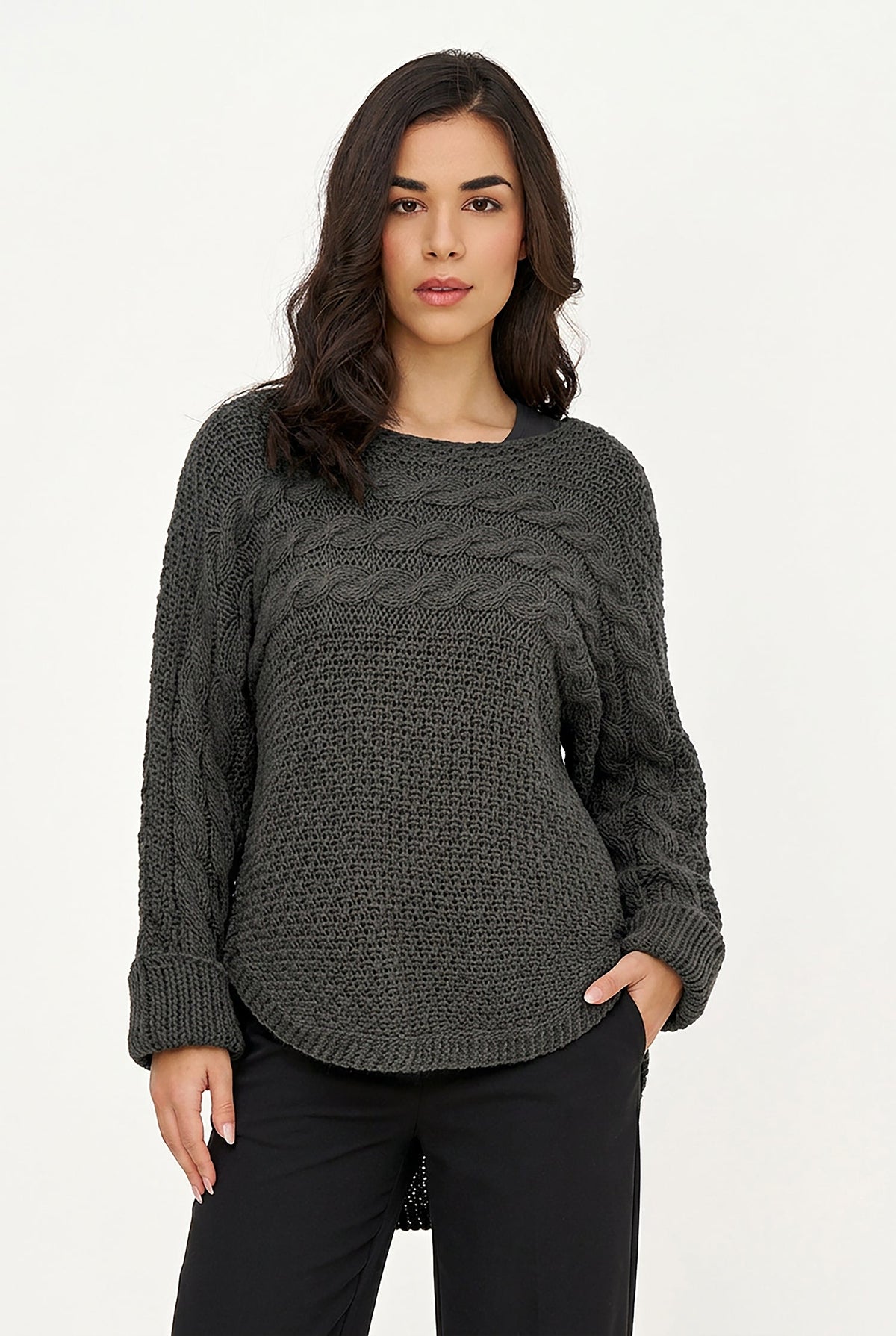 A woman modeling a black cable-knit sweater with a textured waffle-knit body, paired with dark brown pants, against a plain white studio background.