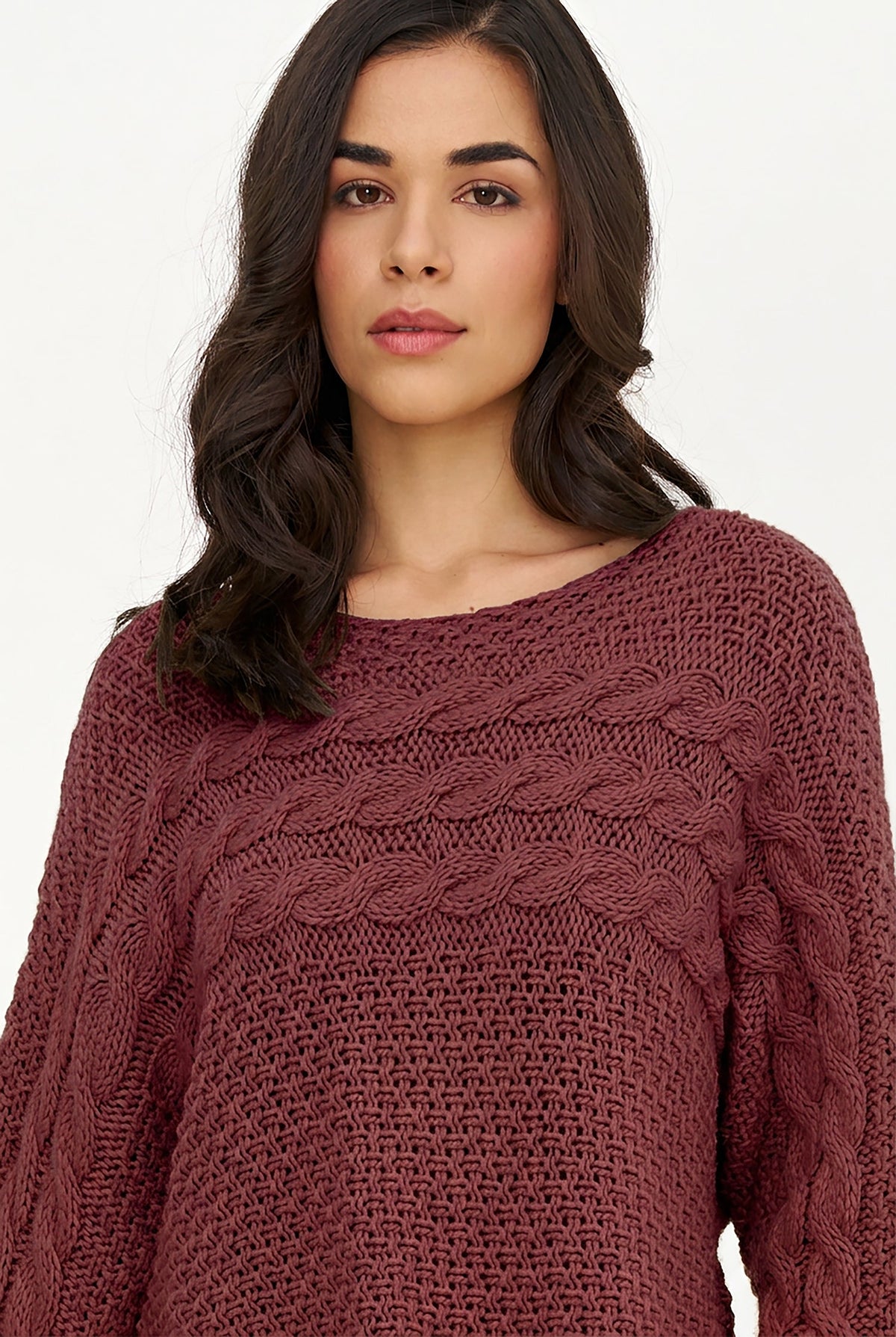 A woman wearing a textured, cable-knit crewneck sweater in a dusty rose or mauve color, shown from the chest up against a plain white background.