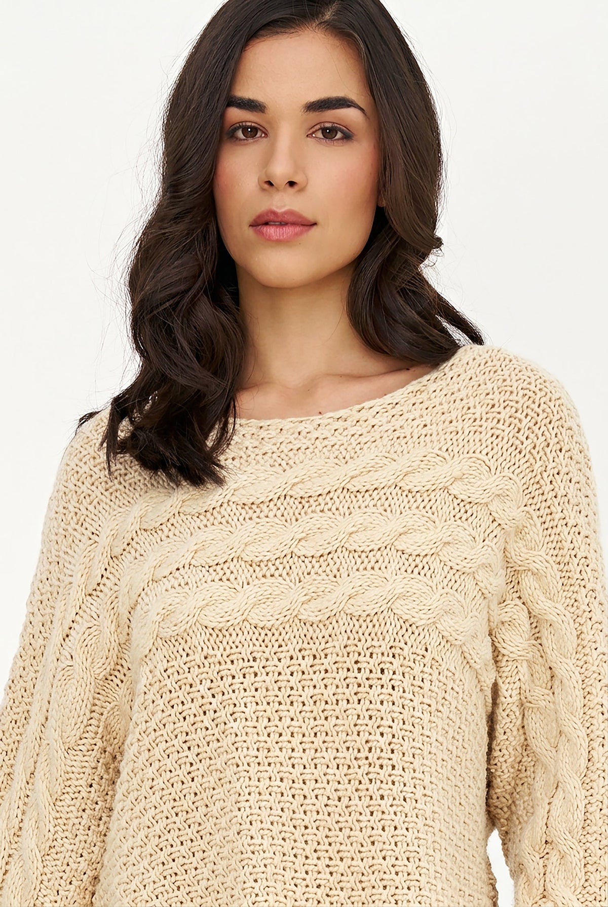 A woman wearing a cream-colored cable-knit sweater against a plain white background.