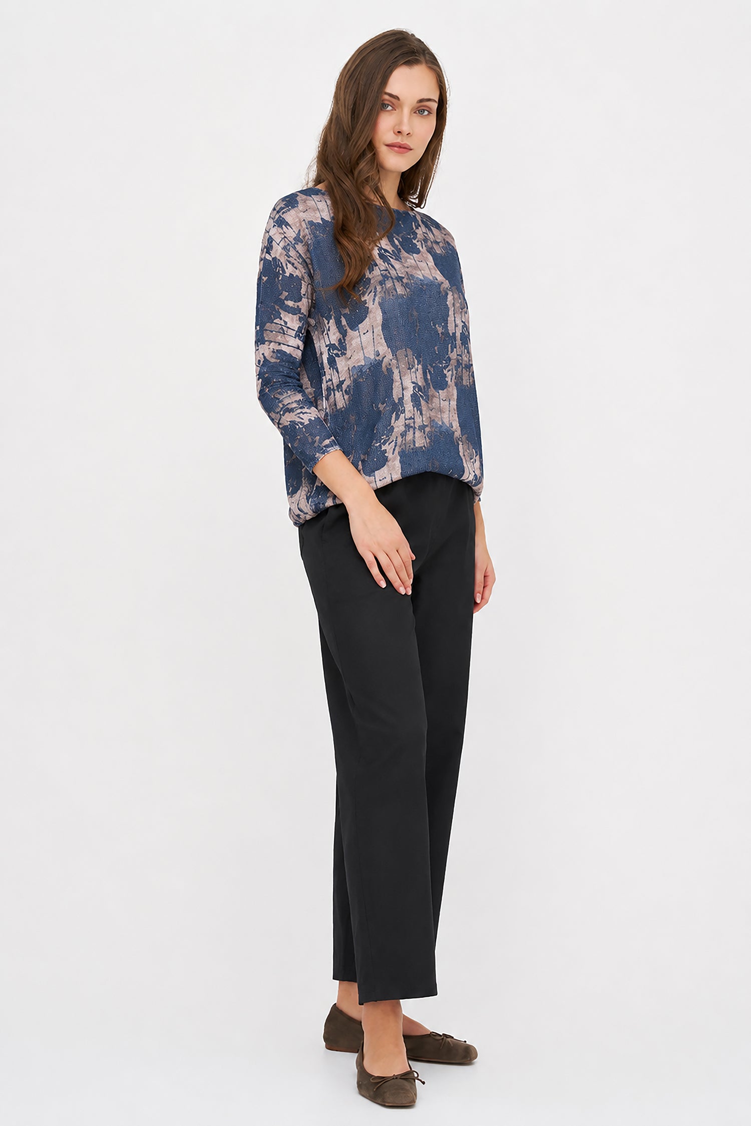 Woman wearing a blue and beige patterned top with black pants on a white background
