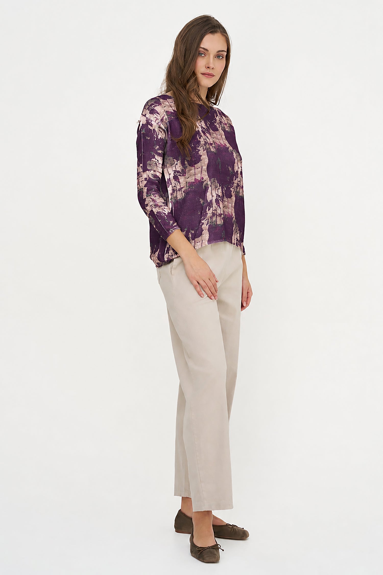 Woman wearing a purple floral blouse and beige pants on a white background