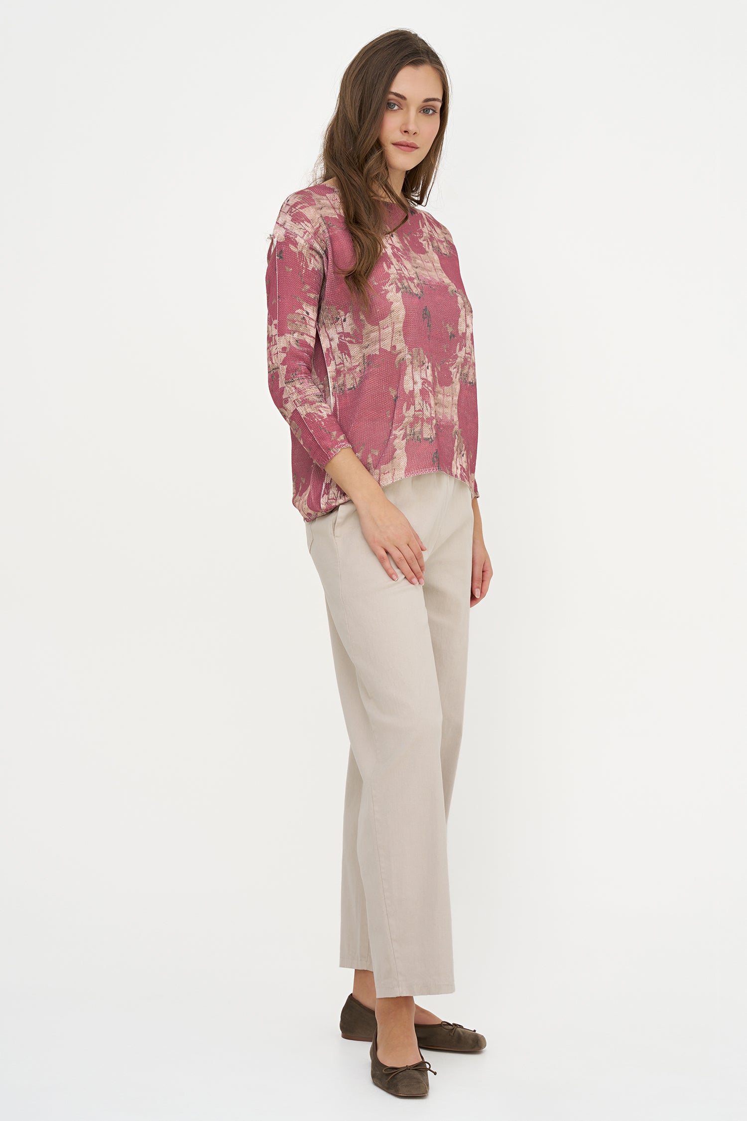 Woman wearing a pink floral blouse and beige pants on a white background