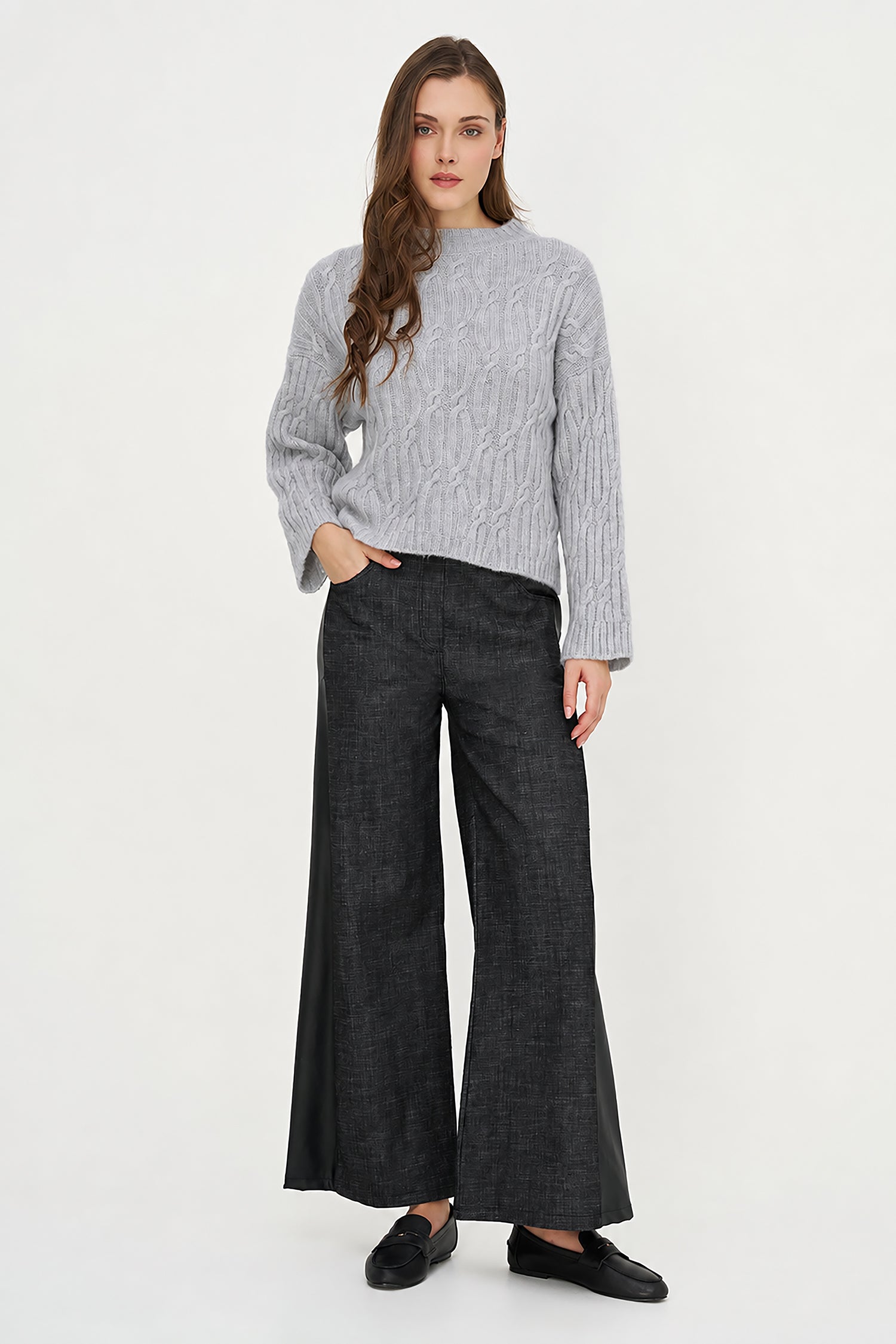 A woman modeling a light gray cable-knit sweater and dark charcoal wide-leg trousers, paired with black loafers, against a plain white studio background.