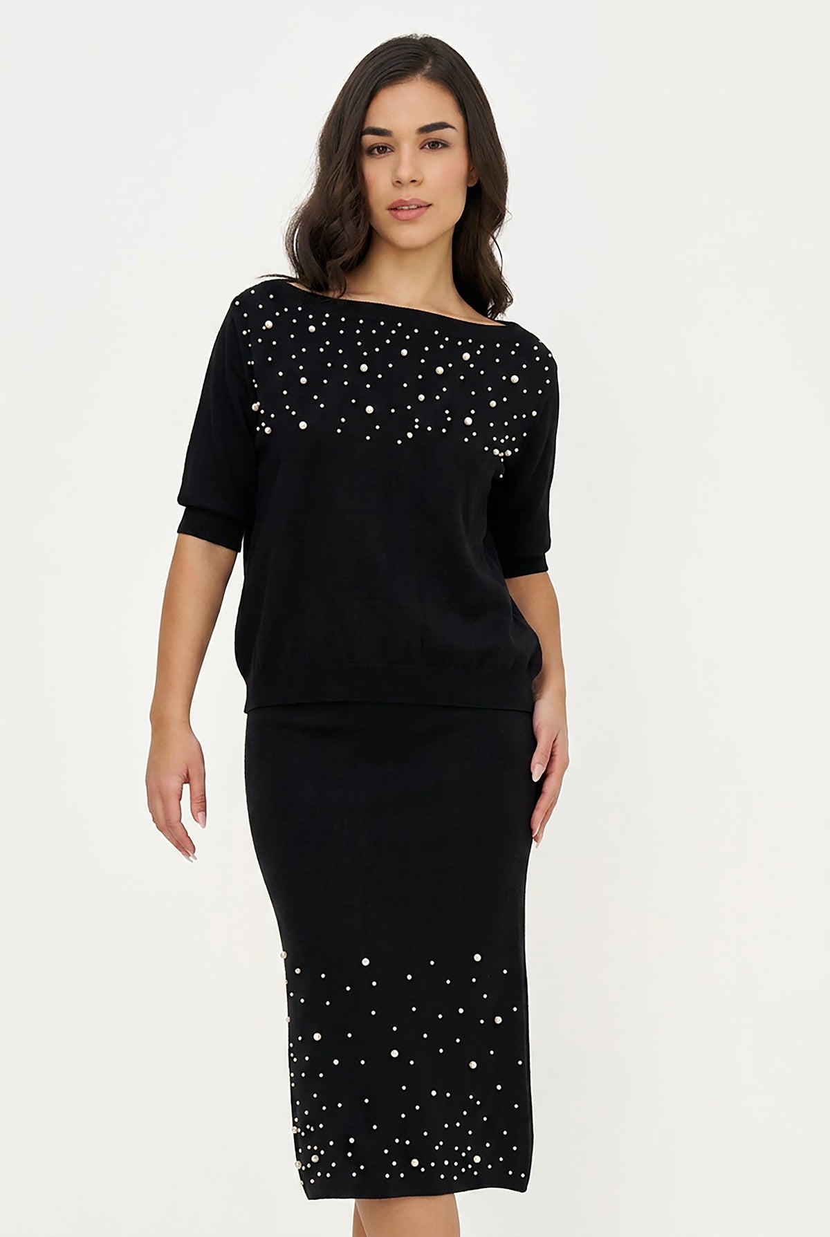 A woman modeling a black off-the-shoulder knit dress with silver rhinestone embellishments across the chest and at the hem, set against a plain white studio background.