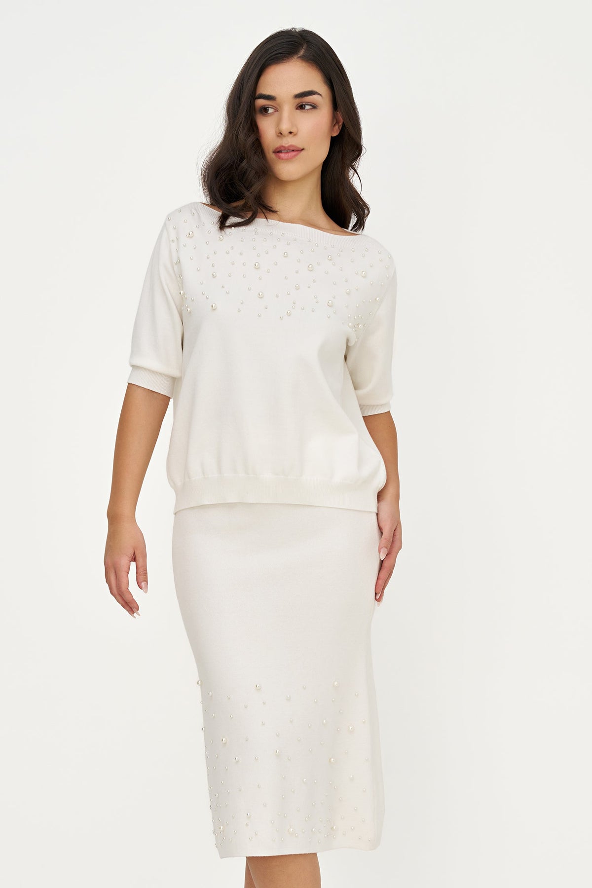 A woman modeling a cream-colored knit two-piece set consisting of a short-sleeve top and a matching pencil skirt, both featuring subtle eyelet embroidery.