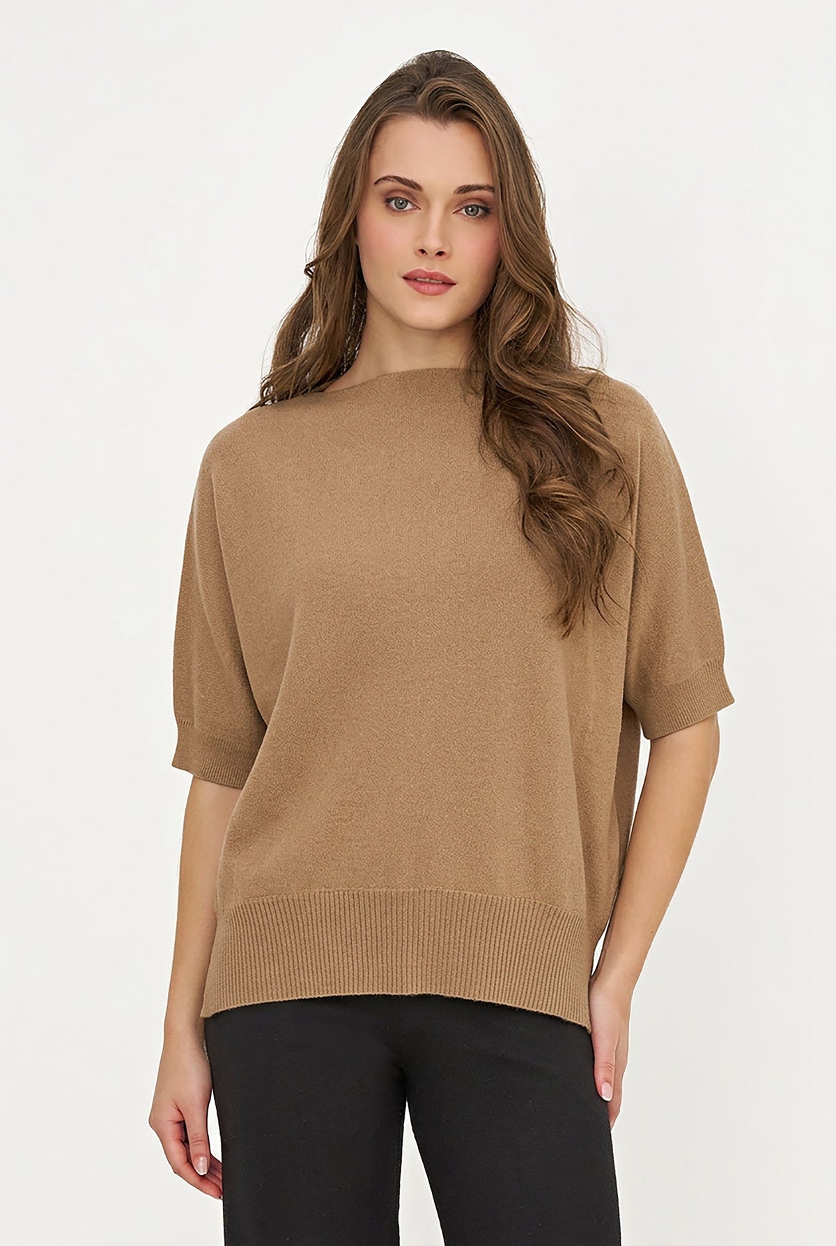 A woman modeling a short-sleeve knit sweater in camel brown, paired with black pants, against a plain white studio background.